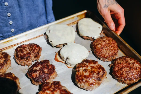 Person holding a sheet pan with cooked, organic, grass-fed beef patties