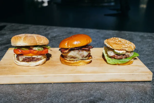 Three finished grass-fed burgers arranged on a wooden cutting board